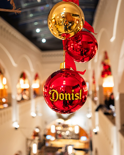 Christbaumkugeln hängen im Bildmittelpunkt. Dahinter der Innenraum von oben in weihnachtlich stimmungsvollen Farben