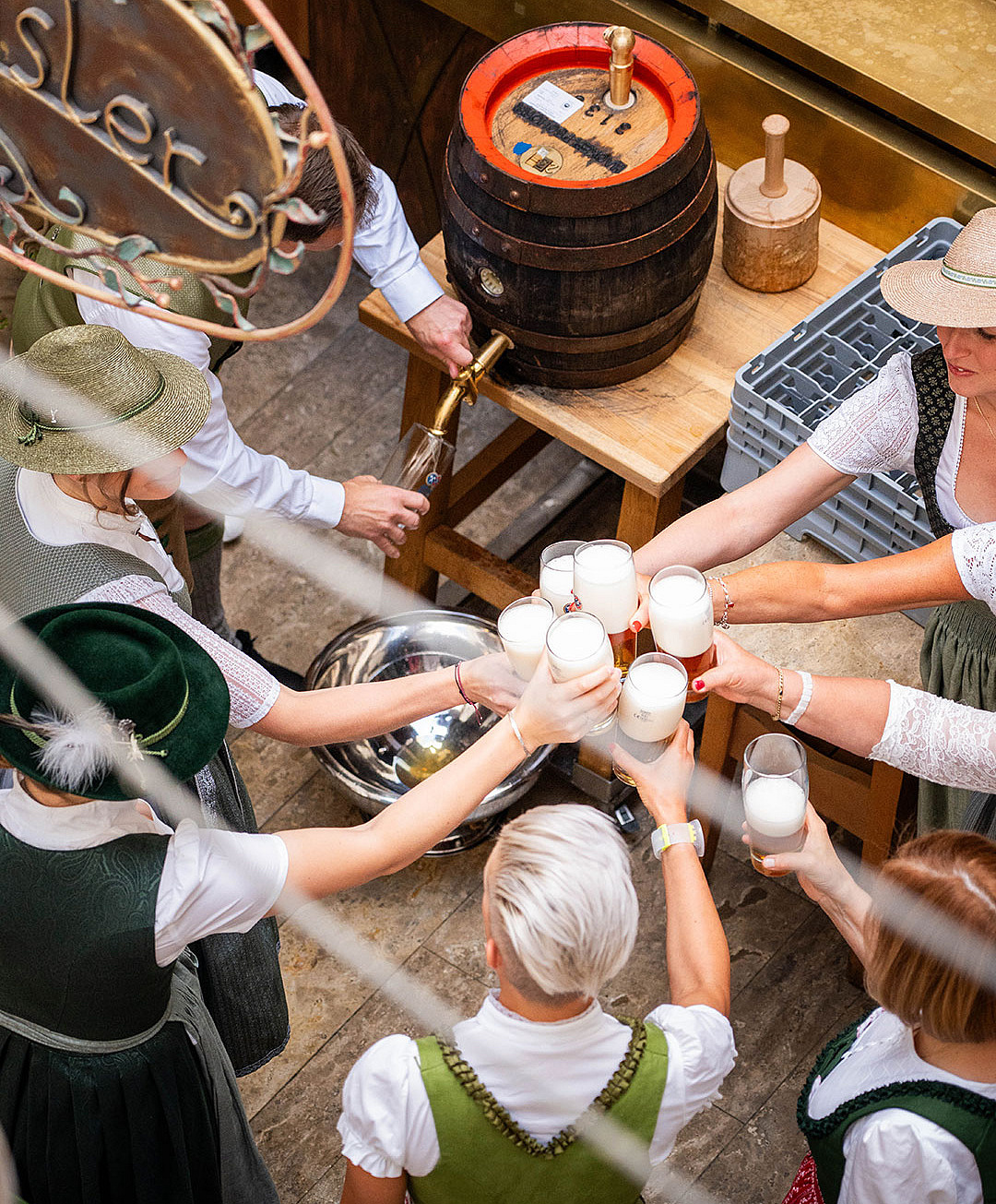 Mehrere Personen stoßen gemeinsam mit frisch gezapften Hacker-Pschorr-Bier aus dem Holzfass an